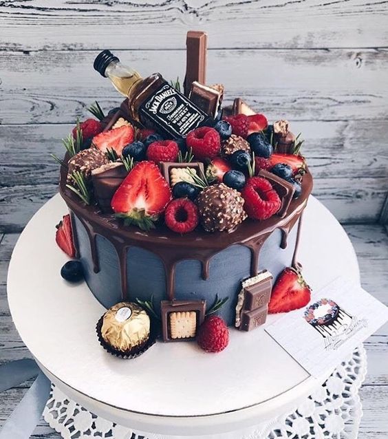 a pretty and cool groom's cake in grey, with chocolate drip, chocolate candies, berries, herbs and a real mini alcohol bottle is amazing
