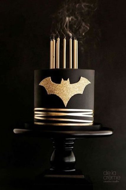 a refined black and gold groom's cake with stripes, a gold glitter bat and gold candles is a perfect idea for a party
