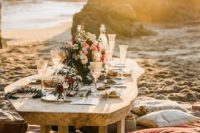 a romantic boho beach wedding picnic space with rugs, pillows, a wicker chest, a low table, bright blooms and candles