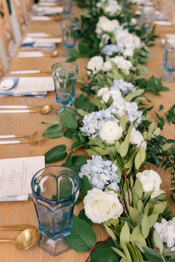 a romantic pastel blue wedding tablescape with blue and neutral blooms, greenery, blue menus and glasses