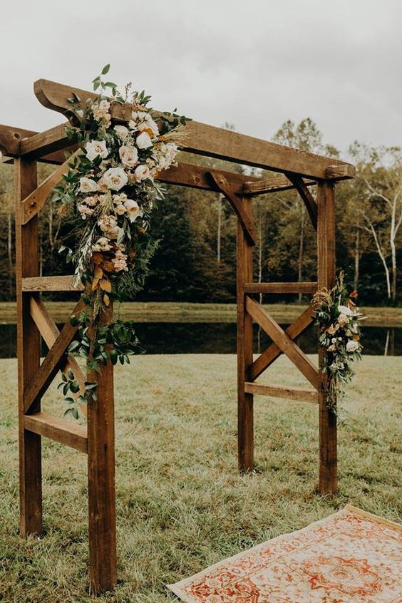 a rustic backyard wedding arch with greenery and blush blooms is a chic idea for a backyard wedding