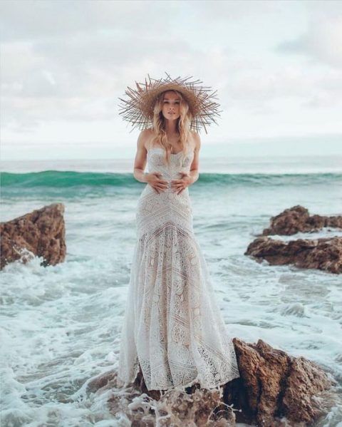 a strapless boho lace fit and flare wedding dress and a fringe straw hat for a fashion-forward bride