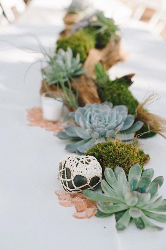 a stylish beach wedding centerpiece of driftwood, succulents, pebbles wrapped in macrame and moss is a unique idea