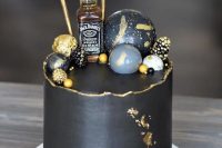 a stylish black and gold groom’s cake with a raw edge, gidled berries, painted spheres, a mini alcohol bottle and gold leaf