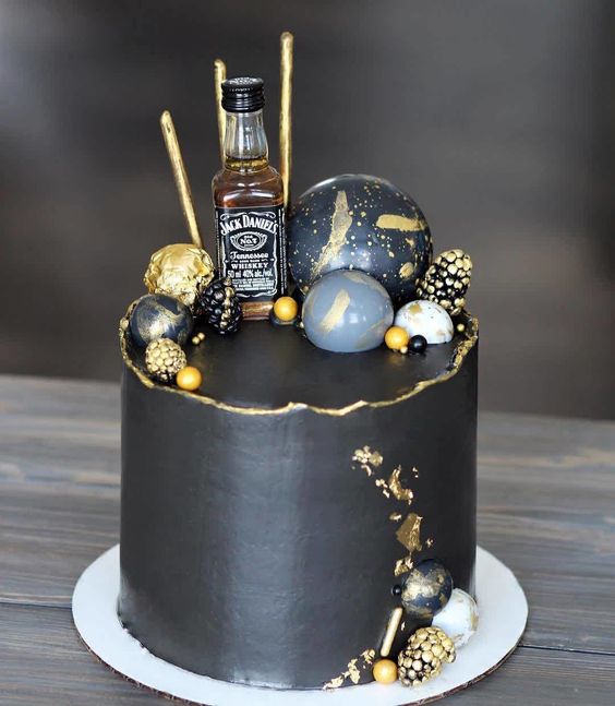 a stylish black and gold groom's cake with a raw edge, gidled berries, painted spheres, a mini alcohol bottle and gold leaf