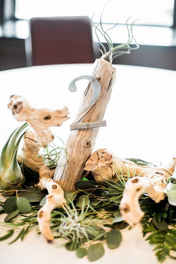 a stylish modern beach wedding centerpiece of driftwood, greenery, air plants and a metal table number