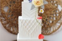 a white textural wedding cake with macrame detailing, pale greenery and super bright blooms on top