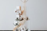 a white wedding cake with cotton, dried succulents, thistles, a hex topper with macrame detailing for a boho wedding