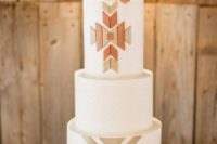 a white wedding cake with geometric patterns, metallic geometric detailing and a sugar skull with a feather on top