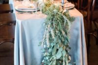 a wild-looking greenery table runner going to the floor and grey canldes plus a greay tablecloth for a chic setup