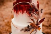an ombre burgundy to white wedding cake with a catchy wreath with berries, feathers, ribbons and a copper base