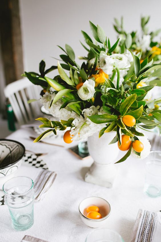a Mediterranean wedding centerpiece of a white urn, white blooms and greenery and kumquats is a great idea for spring or summer