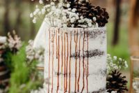 a beautiful and simple semi naked wedding cake with caramel drip, baby’s breath and pinecones for a woodland wedding
