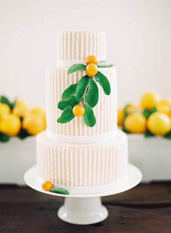 a beautiful striped wedding cake with tan and white stripes and ribbons, with kumquats and leaves for a modern wedding