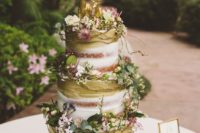 a beautiful woodland wedding cake, partly naked, with greenery, blooms and deer toppers