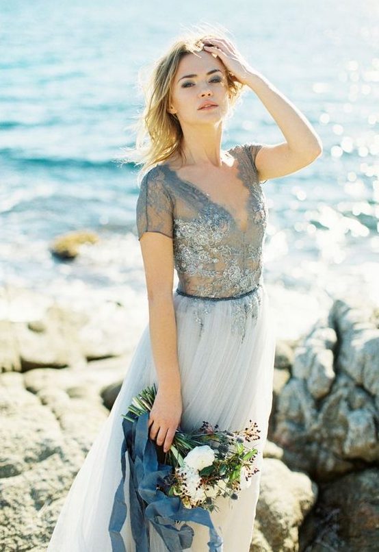 a blue wedding dress with a lace embellished bodice with a V-neckline and short sleeves and a light blue pleated skirt for a beach bride