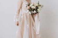 a blush A-line wedding dress with a v-neckline, puff sheer sleeves and white floral appliques for a spring bride