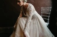 a blush and ivory lace wedding dress with a deep V-neckline and long sleeves and a messy updo with blooms