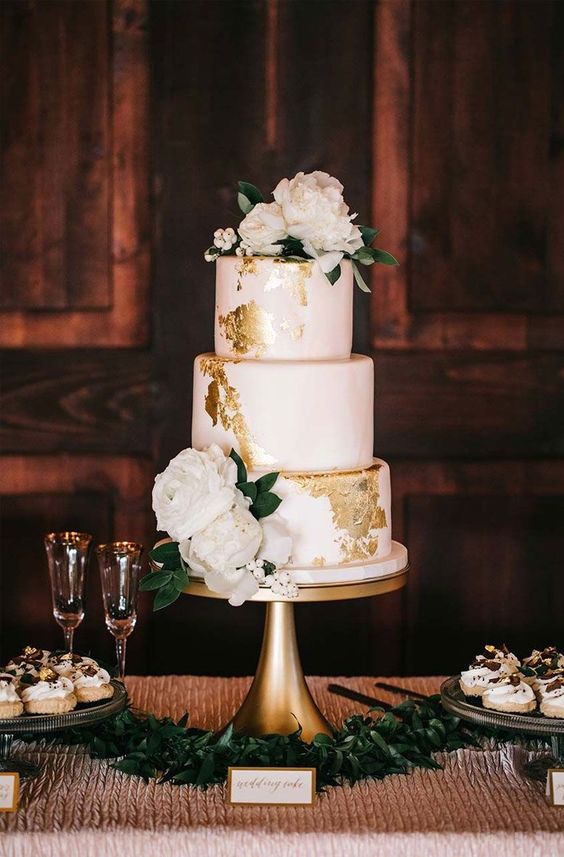 a blush wedding cake with gold leaf decor and fresh white blooms and foliage for a vintage and elegant feel