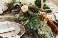 a boho woodland wedding centerpiece with greenery, blooms, berries, antlers and feathers