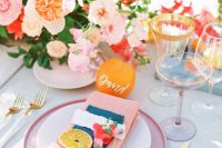 a bold and cheerful tropical wedding tablescape with bright blooms, pink plates and napkins, gold rim glasses and cutlery