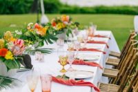 a bold and chic tropical wedding tablescape with bold blooms, pink napkins, colored glasses and tropical leaves