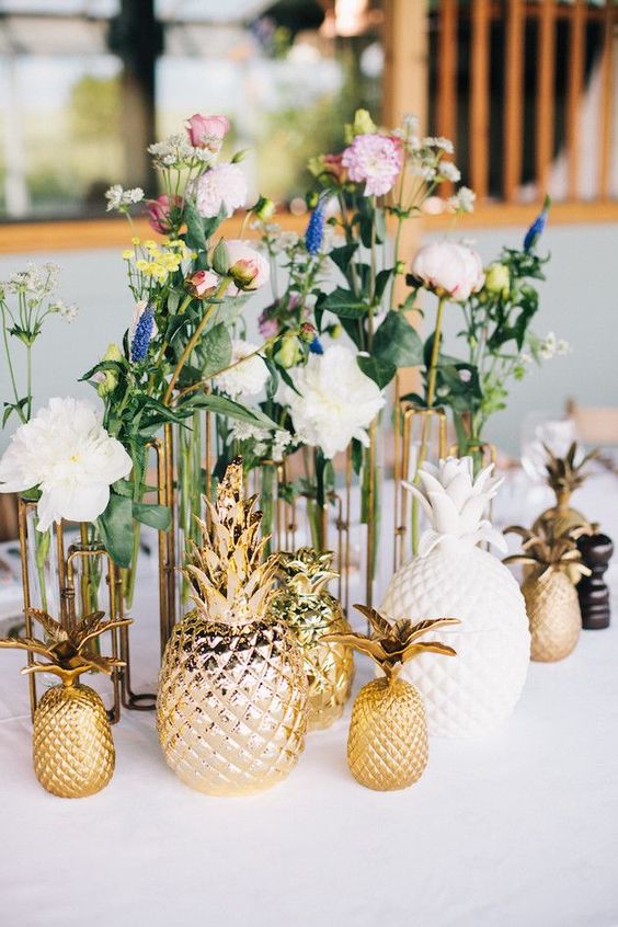 a bold and fun wedding centerpiece of clusters of blooms in various colors and mismatching gold and white pineapples