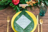 a bold tropical wedding table with a greenery and bright bloom runner, turquoise napkins and yellow plates
