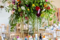 a bold tropical wedding table with a super colorful floral centerpiece on a tall stand, gilded figurines and colored glasses