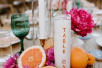 a bold tropical wedding table with bright blooms, fruits and candles plus colored glasses