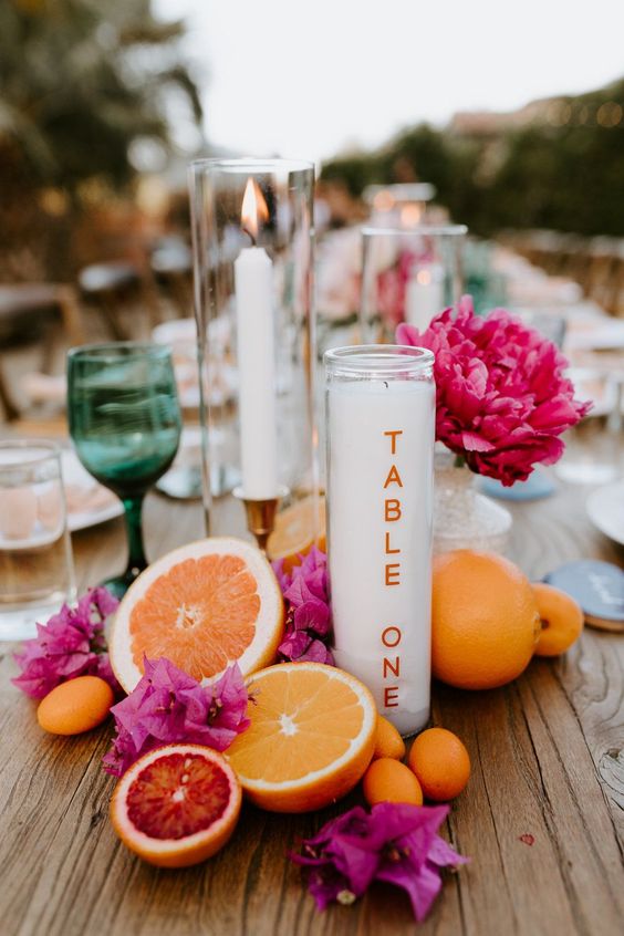 a bold tropical wedding table with bright blooms, fruits and candles plus colored glasses