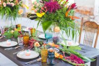 a bold tropical wedding tablescape with colored glasses, a greenery runner and bold floral arrangements