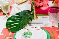 a bold tropical wedding tablescape with pink placemats, green chargers and tropical leaves, pink blooms and gilded palm trees
