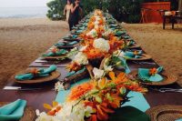 a bright tropical wedding table done in orange, white and blue, with woven chargers and tropical leaves plus driftwood