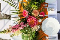 a bright tropical wedding table with a mustard runner, bold blooms, greenery and leaves, white porcelain and candles