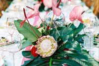 a bright tropical wedding table with a striped pink runner, bold blooms and tropical leaves and a disco ball