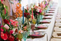 a bright tropical wedding table with bold blooms, greenery, colored glasses and bold stationery and candles