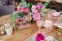 a bright tropical wedding table with bold blooms, pink napkins and glasses, candle lanterns and candle holders gilded inside