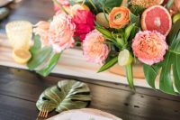 a bright tropical wedding tablescape with muted and bold blooms, tropical leaves, gold cutlery and a blush table runner