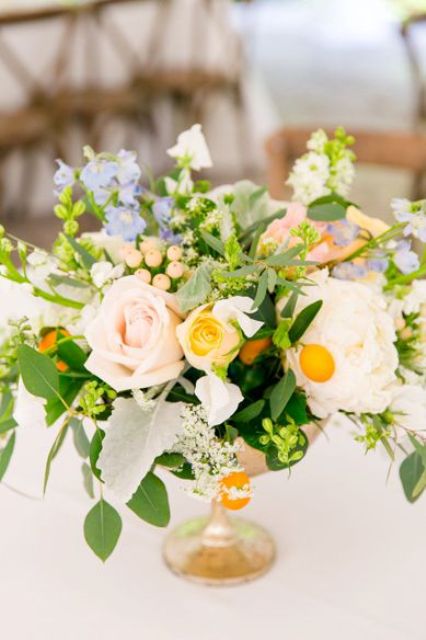 a bright wedding centerpiece of white, blush, blue blooms, greenery, berries and kumquat is amazing for a summer wedding