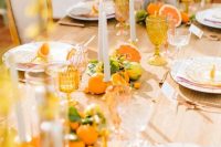 a bright wedding tablescape with various types of fruits including kumquats, tall and thin candles, yellow glasses and colored glass plates