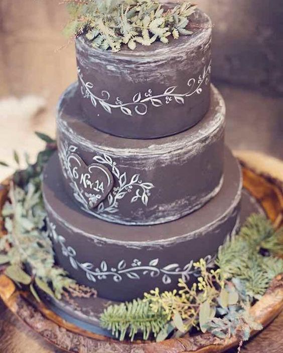 a chalkboard wedding cake with chalking, with a chalkboard heart and some textural greenery on and around the cake