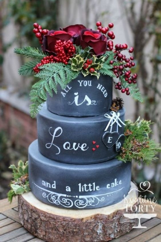 a chalkboard wedding cake with chalking, with greenery, berries and red roses, some ferns and pinecones is a fantastic idea for a Christmas or woodland wedding