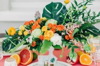 a chic and bold wedding tablescape with a pink tablecloth, bright blooms and greenery, citrus and gold cutlery