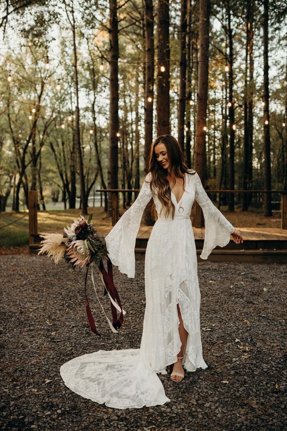 a chic boho lace wedding dress with a deep V-neckline, bell sleeves and a train for a boho woodland bride