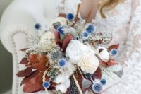 a chic fall wedding bouquet in white, blue, with dried leaves and feathers for a boho bride