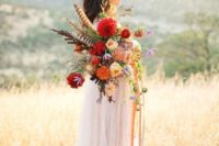 a colorful boho summer wedding bouquet in pink, red, marigold, with greenery, feathers and ribbons