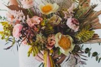 a colorful boho wedding bouquet in pink, mustard, with greenery and twigs plus some ribbons