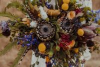 a colorful boho wedding bouquet in yellow, purple, with feathers and greenery is great for a free-spirited bride
