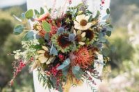 a colorful boho wedding bouquet of yellow blooms, pincushion proteas, thistles, greenery and some little red blooms